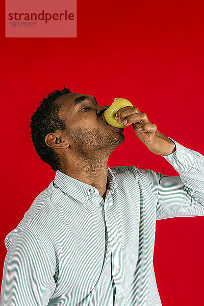 Mann isst Apfel vor rotem Hintergrund