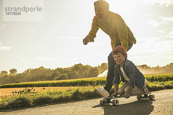 Fröhlicher Enkel  der Spaß hat und vom Großvater Skateboard fährt
