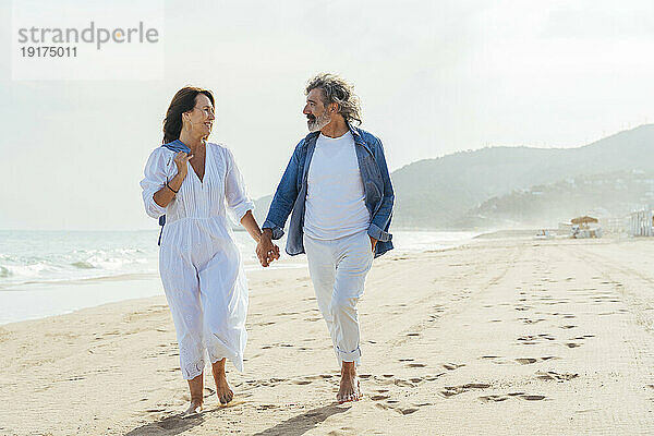 Glückliches älteres Paar hält Händchen und geht am Strand spazieren