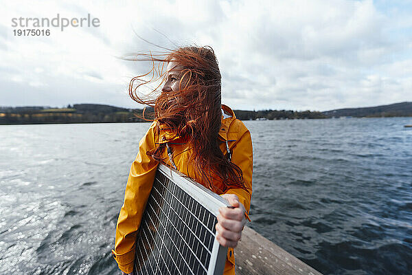 Rothaarige Frau hält Solarpanel am See