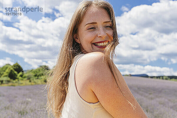 Happy blond woman in front of cloudy sky on sunny day