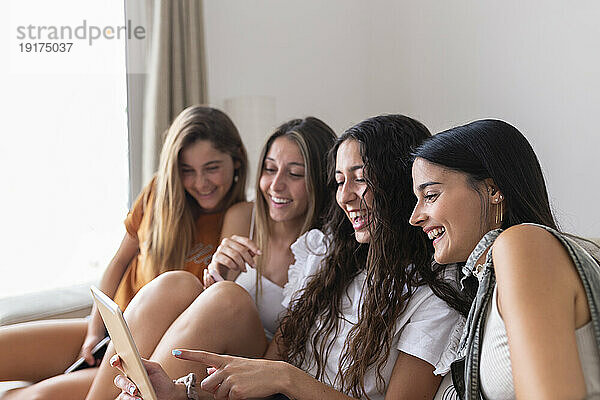 Lächelnde Freunde  die zu Hause einen Tablet-PC nutzen