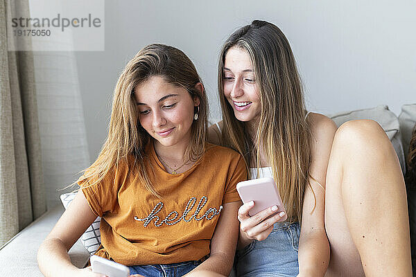 Lächelnde Freunde  die zu Hause ihr Smartphone benutzen