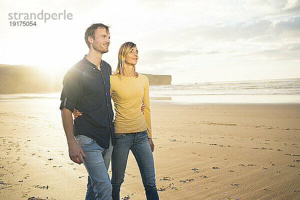Lächelndes Paar  das bei Sonnenuntergang auf Sand spaziert