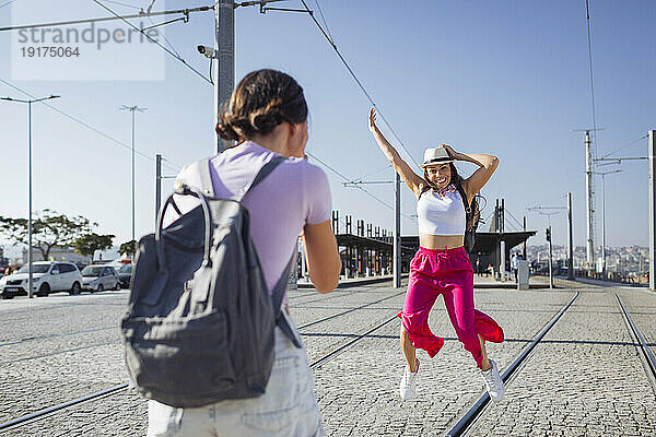 Frau fotografiert Freundin  die auf Straßenbahnschienen springt