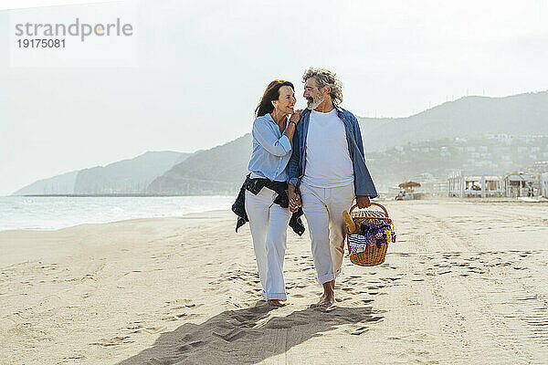 Glückliche Frau umarmt Mann und geht an einem sonnigen Tag mit Korb am Strand spazieren