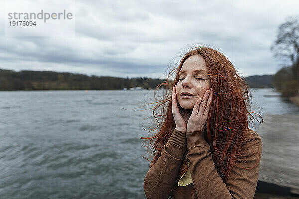Frau berührt Gesicht mit geschlossenen Augen vor dem See