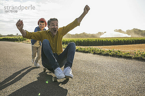 Fröhlicher Mann wird von Enkel auf Skateboard geschoben