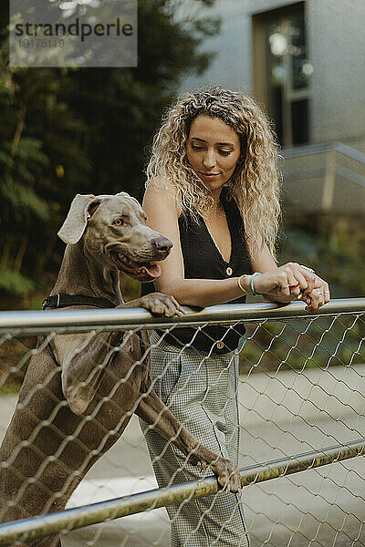 Junge Frau mit Hund steht am Geländer