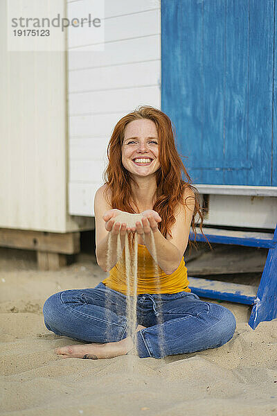 Smiling woman playing with sand at beach on vacation