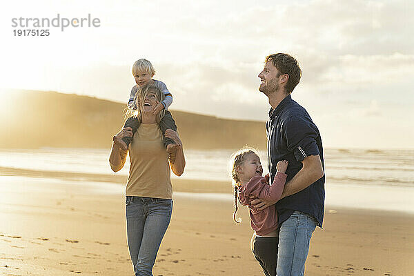 Glückliche Eltern  die mit Kindern am Strand spielen