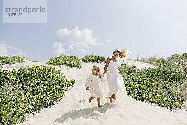 Glückliche Mutter und Tochter laufen am Strand auf Sand