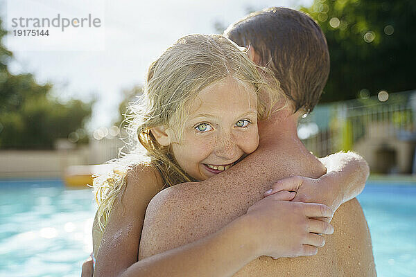 Lächelndes blondes Mädchen umarmt Vater im Schwimmbad