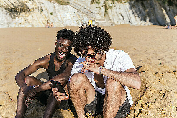 Multiethnische Freunde lachen und schauen an einem sonnigen Tag auf ihr Smartphone