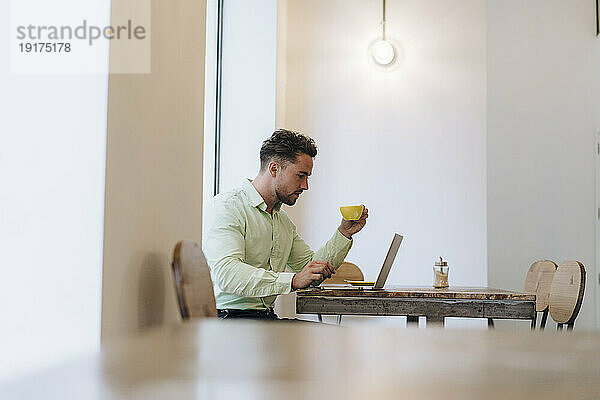 Geschäftsmann arbeitet am Laptop und hält Kaffeetasse im Café