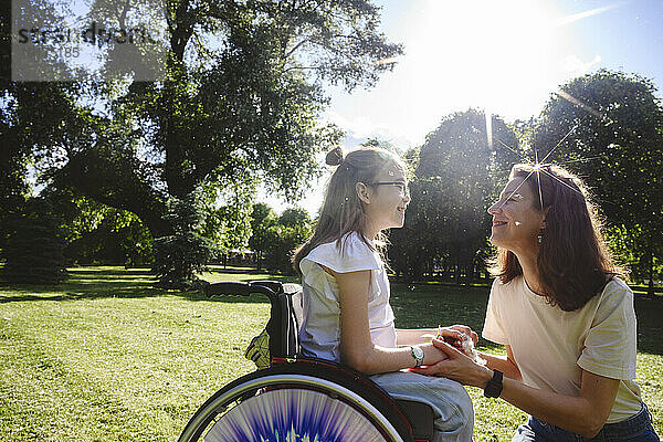 Lächelnde Tochter im Rollstuhl im Gespräch mit Mutter im Park