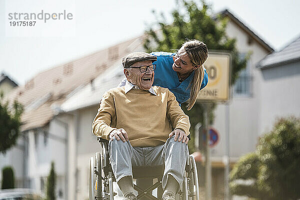 Fröhliche Krankenschwester im Gespräch mit einem älteren Mann  der im Rollstuhl sitzt