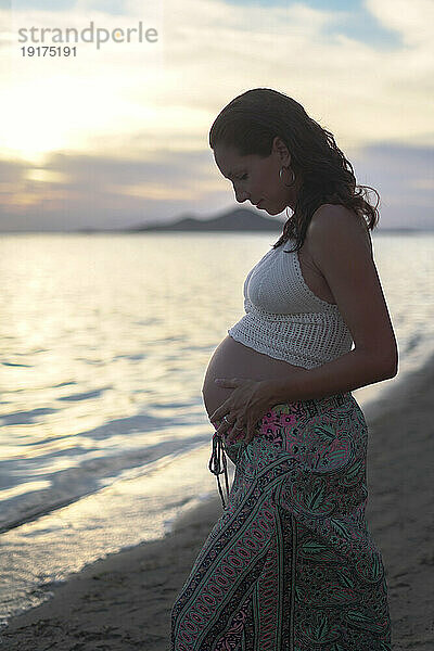 Schwangere Frau berührt Bauch am Strand