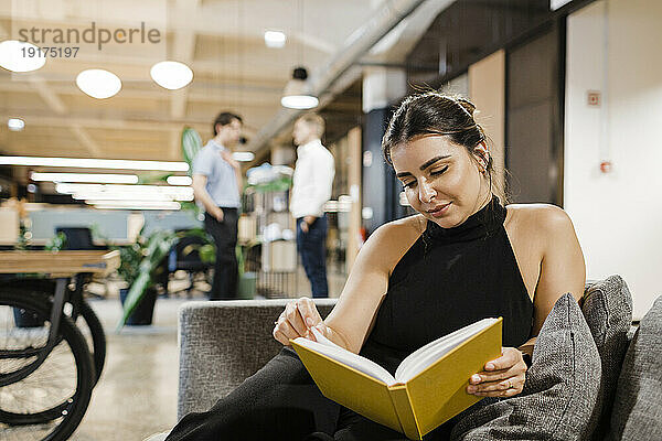 Geschäftsfrau liest Buch auf Sofa im Büro