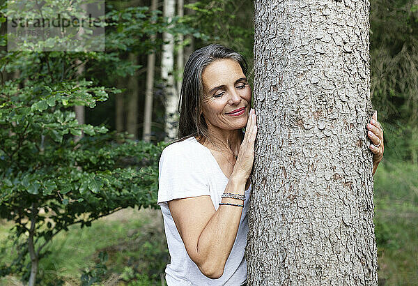 Lächelnde Frau umarmt Baum im Wald