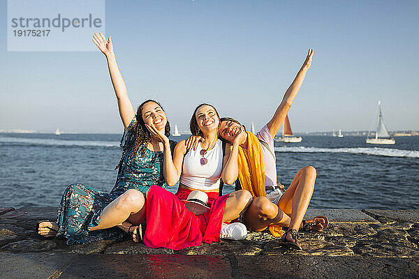 Fröhliche Freunde sitzen zusammen auf der Promenade am Wasser