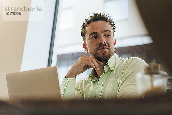 Junger Geschäftsmann mit Laptop sitzt im Café