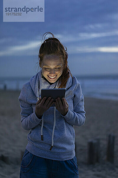 Lächelnde Frau nutzt Tablet-PC am Strand im Urlaub