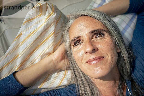 Lächelnde Frau mit grauen Haaren entspannt sich an einem sonnigen Tag