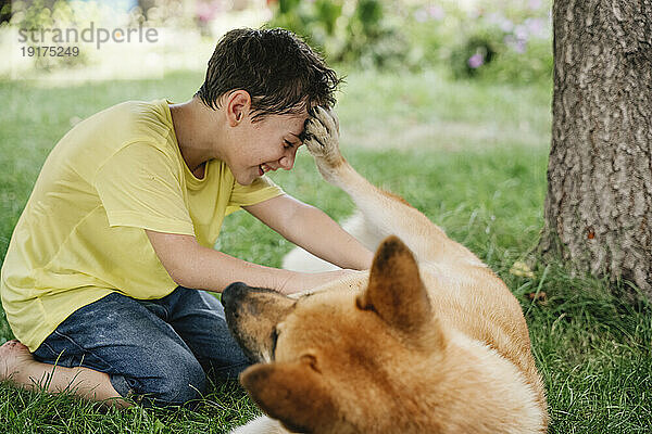 Happy boy playing with dog lying on grass in backyard