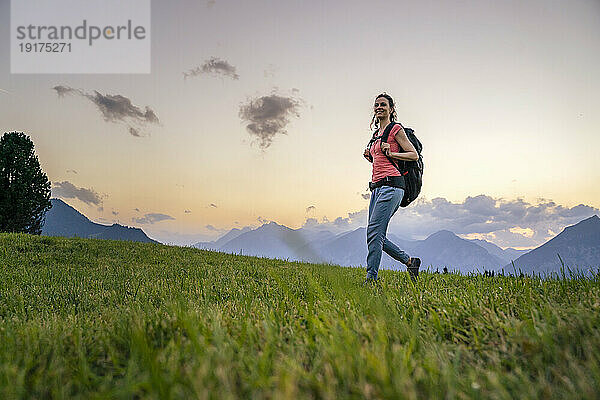 Woman with backpack hiking in meadow at sunset
