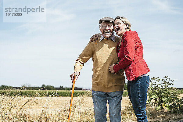Cheerful woman embracing elderly man standing by field