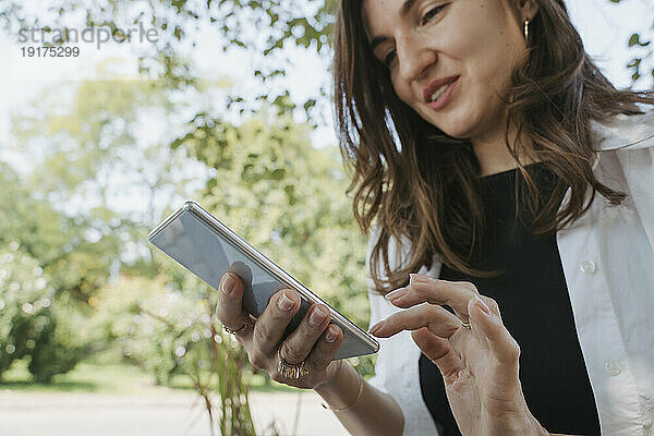 Lächelnde Geschäftsfrau benutzt Smartphone im Garten