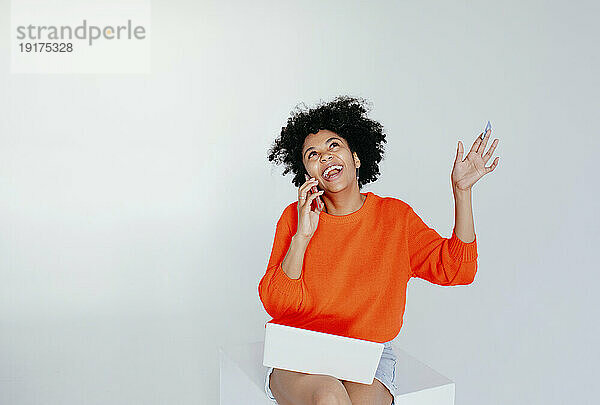 Glückliche junge Frau mit Laptop  die vor weißem Hintergrund auf dem Handy spricht