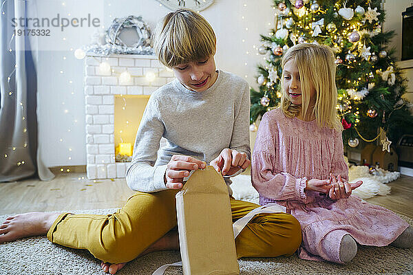 Boy opening Christmas present by sister in living room
