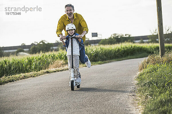 Happy man enjoying riding push scooter with grandson on street