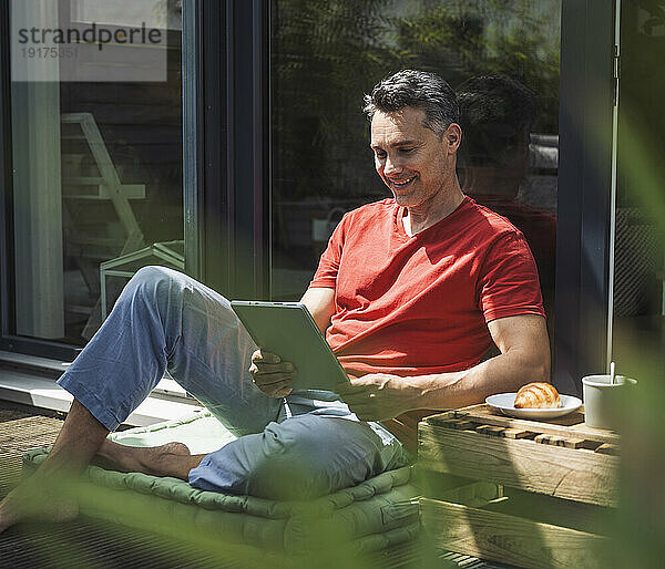 Mann entspannt sich auf Balkon mit digitalem Tablet in der Hand