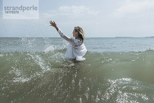 Frau mit erhobener Hand spritzt Wasser im Meer