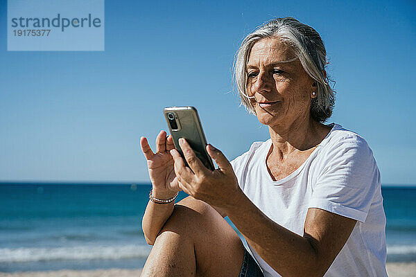 Lächelnde Frau benutzt Smartphone am Strand