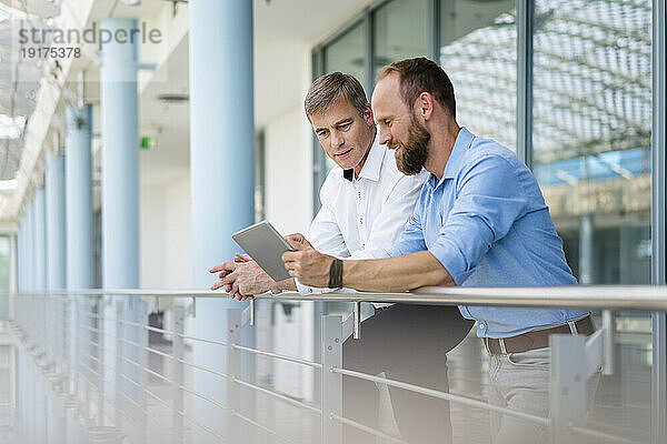 Kollegen unterhalten sich im Bürogebäude mit einem digitalen Tablet