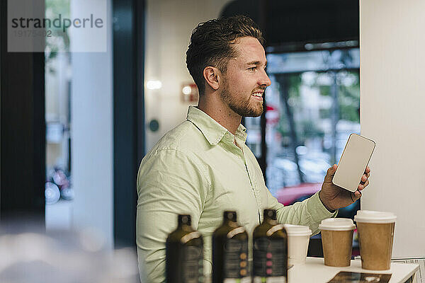 Lächelnder junger Geschäftsmann mit Smartphone im Café