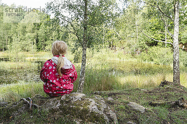 Mädchen sitzt in der Nähe eines Sees im ruhigen Wald