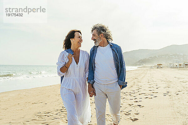 Glückliche ältere Männer und Frauen  die an einem sonnigen Tag unter freiem Himmel am Strand spazieren gehen