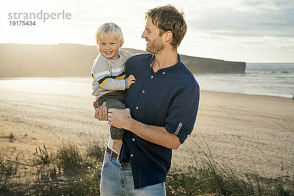 Glücklicher Vater trägt Sohn am Strand