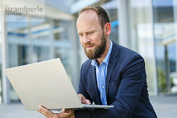 Businessman sitting in front of office building using laptop