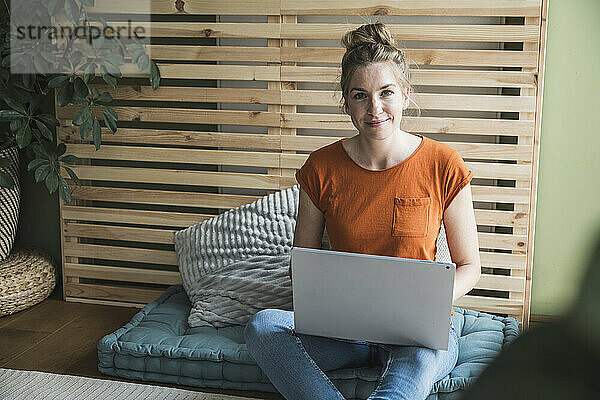 Porträt einer Frau  die mit einem Laptop auf einer Matratze sitzt