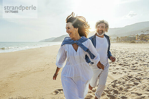 Fröhliches älteres Paar hält Händchen und läuft am Strand
