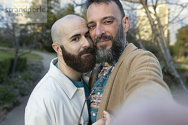 Lächelndes schwules Paar  das bei Sonnenuntergang ein Selfie im Park macht
