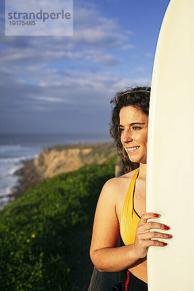 Lächelnde Frau mit Surfbrett an einem sonnigen Tag am Strand