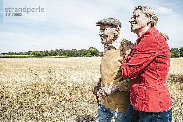 Lächelnde Frau geht an einem sonnigen Tag mit einem älteren Mann spazieren