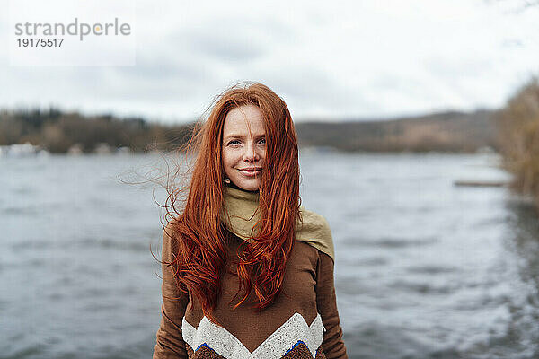 Lächelnde rothaarige Frau mit langen Haaren vor dem See